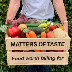 Brightly coloured vegetables fill a wooden crate emblazoned with the words Matters of Taste