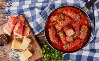 delicious Italian Braciole - beef steak rolls filled with sliced prosciutto, grated parmesan cheese and parsley, cooked with marinara sauce in a skillet, ingredients at the background, view from above