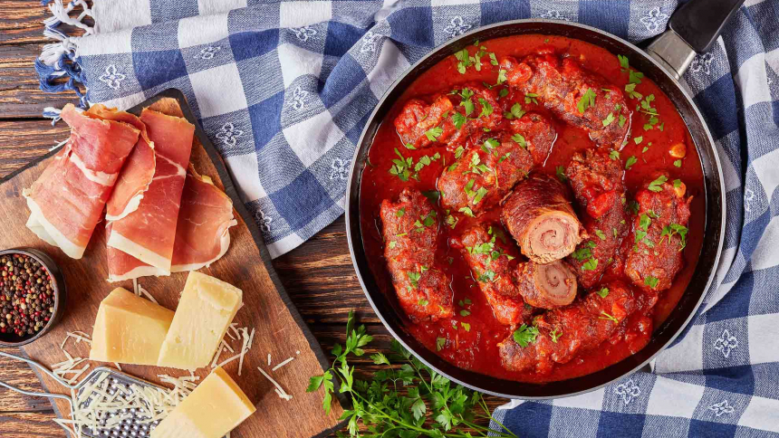 delicious Italian Braciole - beef steak rolls filled with sliced prosciutto, grated parmesan cheese and parsley, cooked with marinara sauce in a skillet, ingredients at the background, view from above
