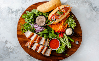 a brown wooden platter with DIY pork belly banh mi ingredients such as bread and carrots