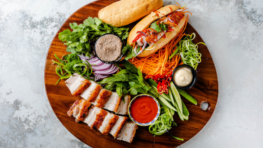 a brown wooden platter with DIY pork belly banh mi ingredients such as bread and carrots